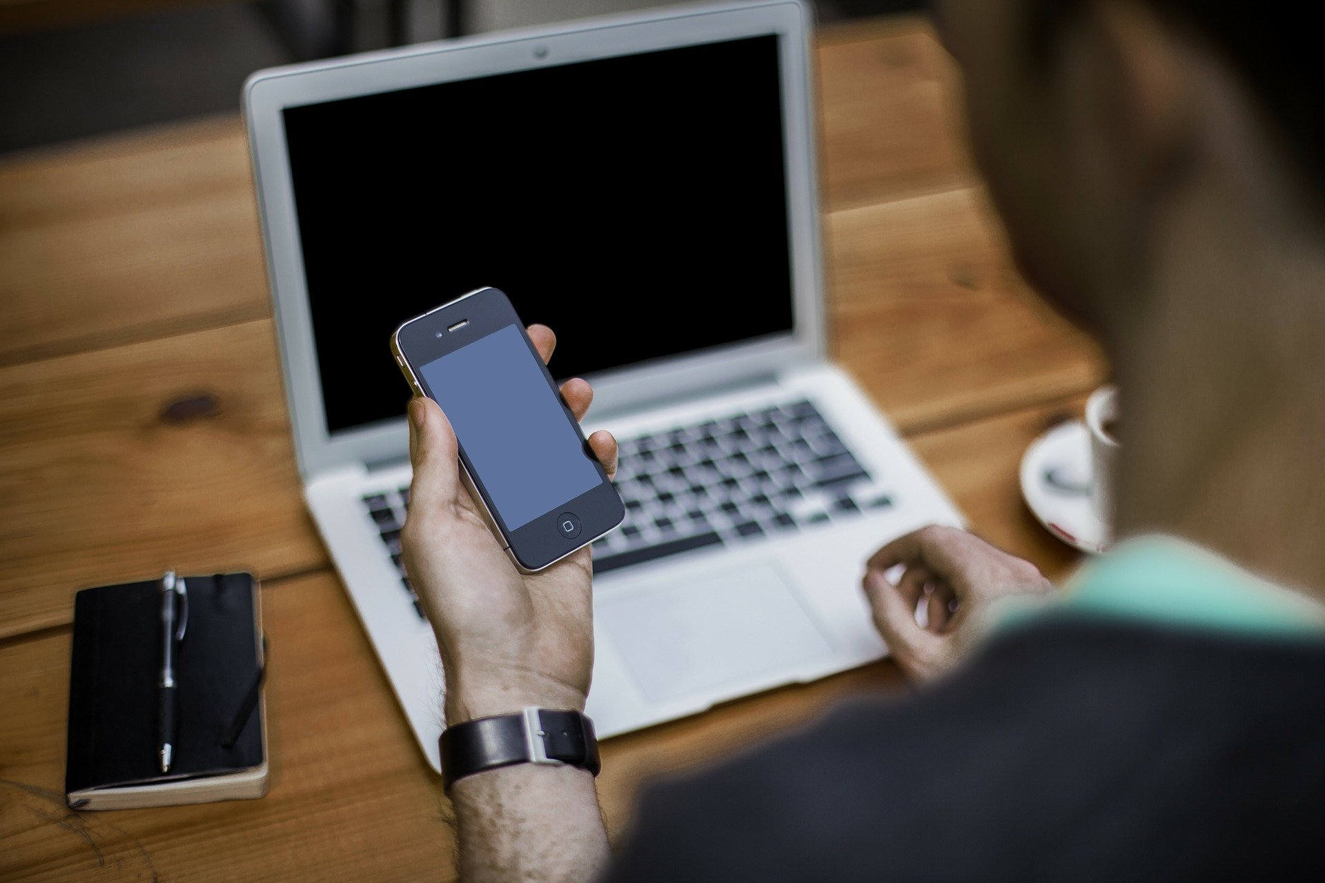 blogger mit Smartphone in der linken Hand sitzend vor seienem Laptop